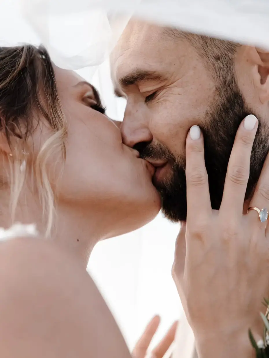 A couple kissing beneath the veil, the bride's hand resting on his cheek