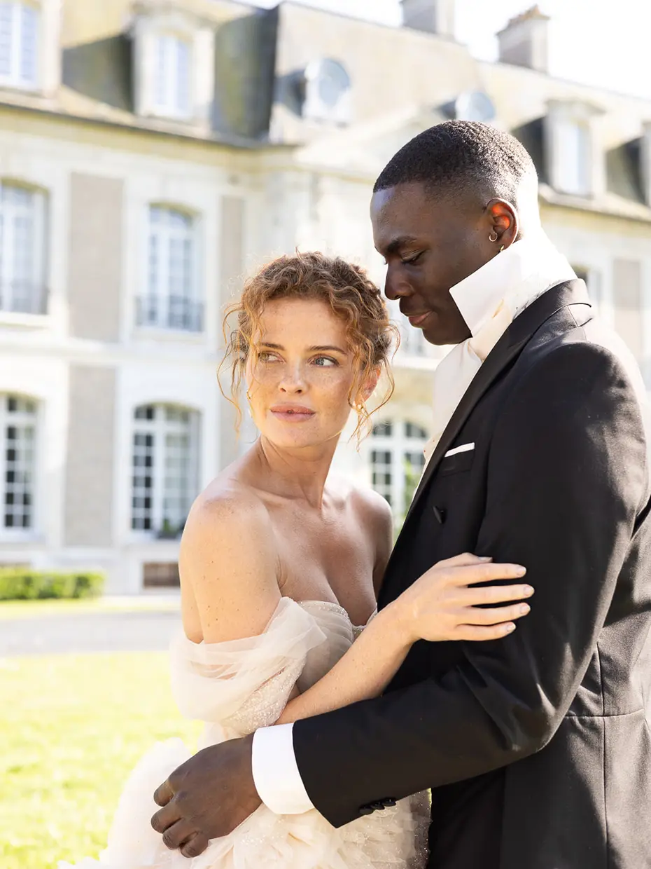 A couple embracing in front of a chateau facade, the bride in a soft white gown
