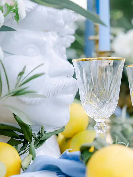 Table setting detail: a sculpted white linen napkin, a crystal glass rimmed with gold, lemons and a blue candle