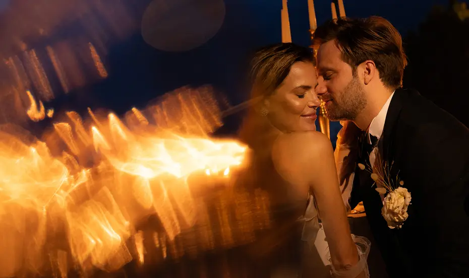 A couple forehead to forehead after dark, firelight blurring in the foreground