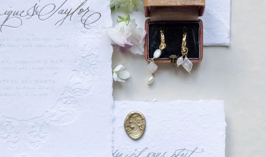 Calligraphed wedding stationery, a jewellery box holding earrings and a gold wax seal on textured paper