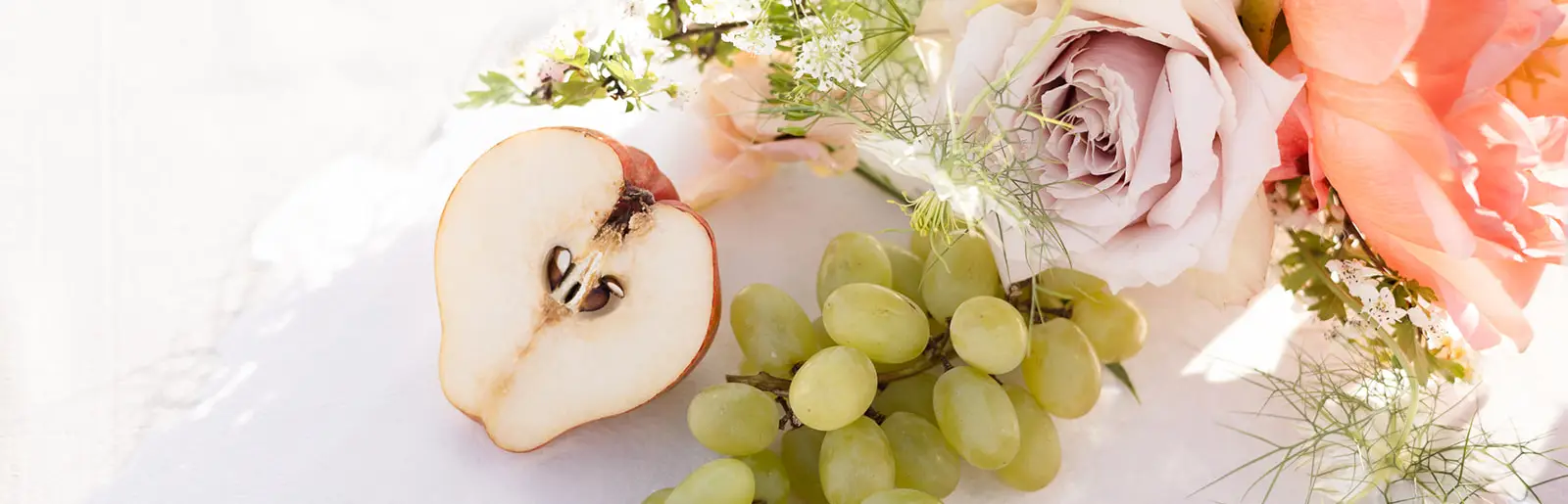 A tablescape detail at Château Diter: grapes, a halved pear and pale roses on white linen.