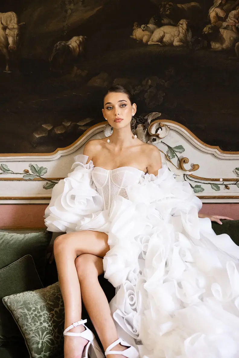 A bride seated in a period armchair, her tulle skirt spread around her.