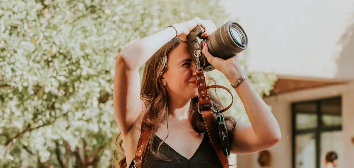 A photographer at work, camera raised, among the tables of an outdoor reception.