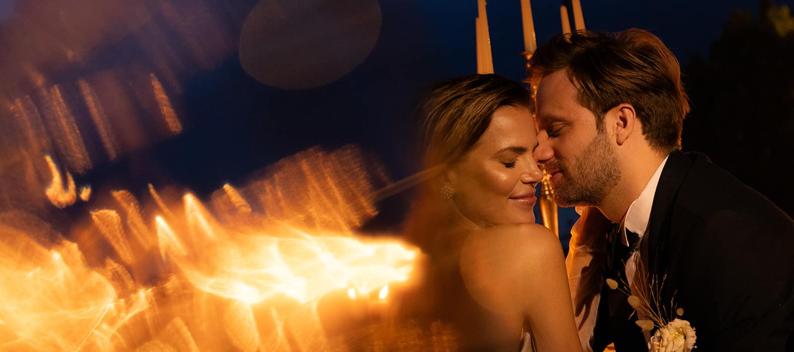 Bride and groom after dark, almost touching, the evening's firelight streaking past in the foreground.