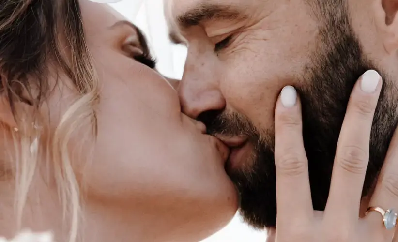 A couple kissing beneath the veil, the bride's hand resting on his cheek.