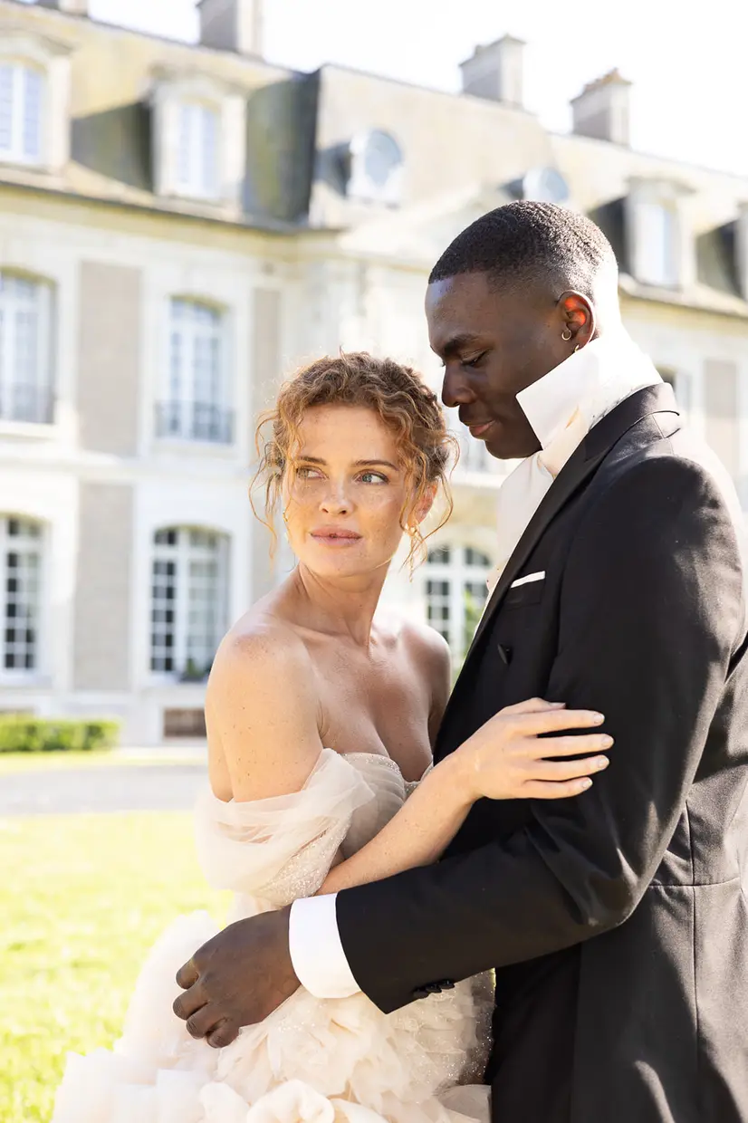 A couple embracing in front of a château façade, the bride in a soft white gown.